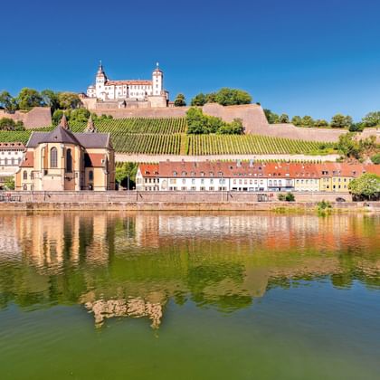 Festung Marienberg fort op een heuvel met wijngaarden in Würzburg, weerspiegeld in de Main. Kleurrijke gebouwen langs de waterkant.