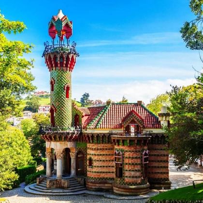 El Capricho van Gaudí in Comillas met een kleurrijke cilindrische toren met groene tegels en sierlijke versieringen, omgeven door weelderige bomen.