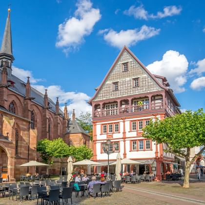 Middeleeuws stadsplein in de Palts met gotische kathedraal, vakwerkhuizen, café-terras en blauwe lucht met witte wolken.