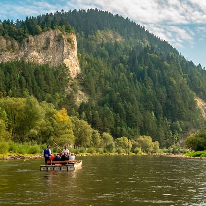 Traditioneel houten vlot met passagiers op de Dunajec rivier omgeven door beboste bergen en dramatische kalkstenen kliffen.