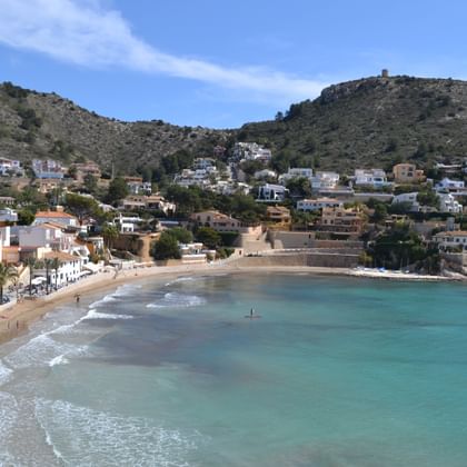 Costa Blanca strandbaai met turquoise water Schilderachtige kustbaai aan de Costa Blanca met turquoise water, zandstrand, witte gebouwen langs de kust en heuvels met huizen onder blauwe lucht.