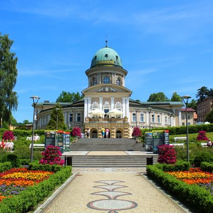 Historisch sanatorium met groene koperen koepel in Lądek-Zdrój. Formele tuinen met kleurrijke bloemperken langs het pad naar de hoofdtrap.