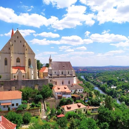 Kasteelcomplex Znojmo in Moravië, Tsjechië, met witte kerk en vestingmuren boven een rivierdal met groene bossen.