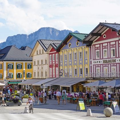 Mondsee stadscentrum met kleurrijke historische gebouwen, terrasjes, voetgangers en fietsers. Bergen zichtbaar op de achtergrond.