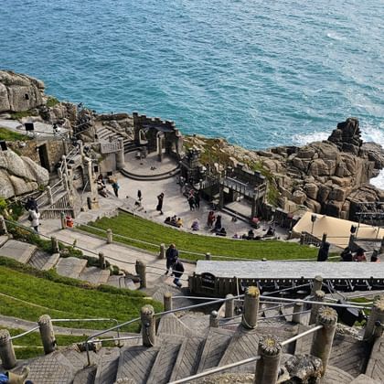 Minack Theatre in Porthcurno, Cornwall: openlucht amfitheater in rotsen uitgehouwen met stenen trappen en podium boven turkooizen zee.