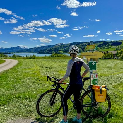 Vrouwelijke fietser met gravelbike en helm bij informatiebord met uitzicht op Irrsee meer in Oostenrijkse Salzkammergut regio.