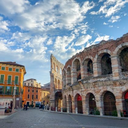 Oud Romeins amfitheater Arena van Verona met roze en witte stenen bogen. Kleurrijke gebouwen omzomen het geplaveide plein onder een blauwe lucht met wolken.