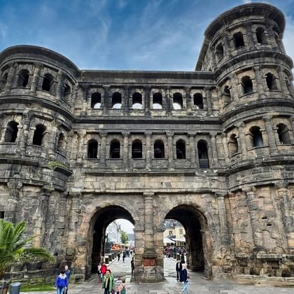 Porta Nigra, oude Romeinse stadspoort in Trier met donkere zandstenen muren, twee ronde torens en meerdere bogen. Bezoekers lopen onder de poort.