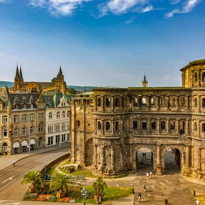 Porta Nigra, oude Romeinse stadspoort in Trier met verweerde zandstenen bogen. Historische gebouwen en kerktorens zichtbaar op achtergrond.