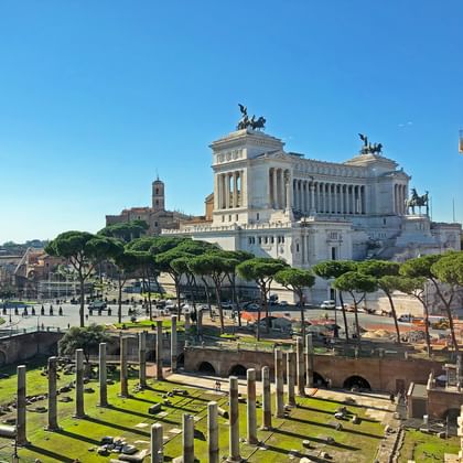 Monumento a Vittorio Emanuele II in Rome met witte marmeren zuilen en standbeelden, uitkijkend over antieke Romeinse ruïnes met stenen zuilen.