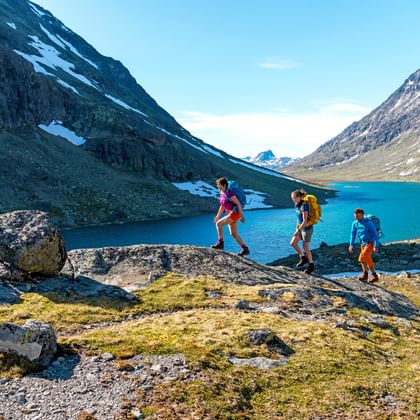 Vier wandelaars steken rotsachtig terrein over naast een turquoise bergmeer in Svartdalen vallei, omringd door steile bergen en sneeuwvlekken.