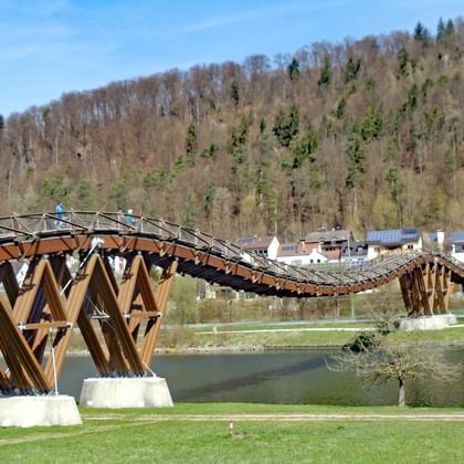 Gebogen houten brug Essing over een rivier in Natuurpark Altmühltal, met beboste heuvels en dorpshuizen op de achtergrond.