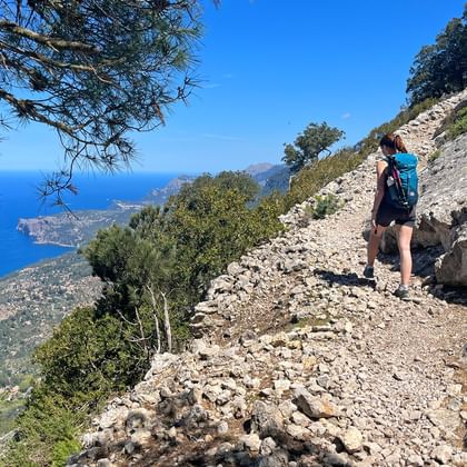 Wandelaarster met rugzak op rotsachtig pad van GR221 op Mallorca met uitzicht op Middellandse Zee en kustlijn.