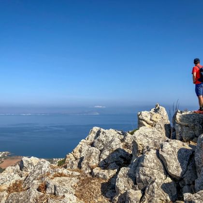 Wandelaar in rood shirt met rugzak staat op rotsachtige kalksteenklif met uitzicht op de Middellandse Zee aan Mallorca's oostkust.
