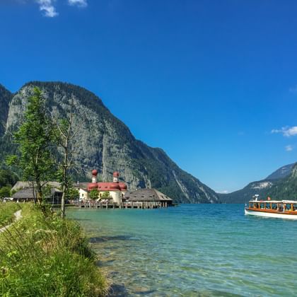 St. Bartholomae kerk met rode uikoepels aan de oever van het Koenigssee meer, omringd door steile Alpengebergte en helder water.
