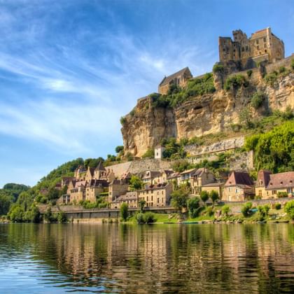 Middeleeuws dorp met stenen kasteel op kalkstenen klif boven kalme Dordogne in Périgord. Traditionele huizen dalen af naar de waterkant.