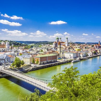Panoramisch uitzicht op Passaus historische oude stad langs de Donau met kleurrijke gebouwen, kerktorens en een brug onder blauwe lucht.