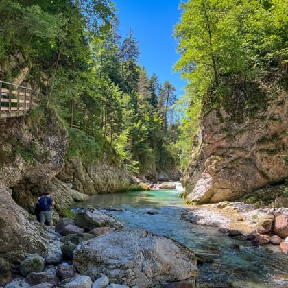 Houten brug over een kristalheldere bergrivier met turquoise water stromend tussen rotsachtige kliffen omgeven door weelderig groen bos.