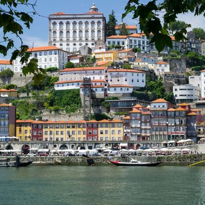 Zicht op Porto's historische heuvel met kleurrijke gebouwen langs de Douro. Traditionele boten liggen aangemeerd aan de waterkant.