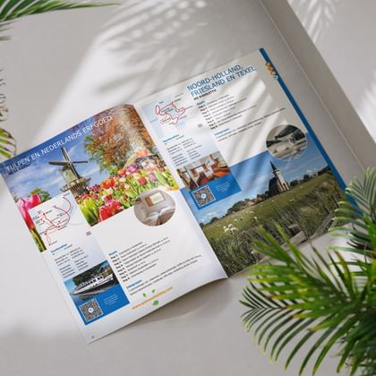Open reisbrochure met fietsroutes in Holland, tulpenvelden, molen en kaarten. Groene palmbladeren omlijsten het witte oppervlak.