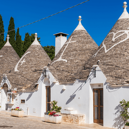 Rij traditionele trulli huizen in Alberobello met kenmerkende kegelvormige stenen daken, witte muren en houten deuren onder blauwe hemel.