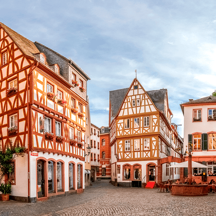 Geplaveide plein in Mainz omringd door kleurrijke vakwerkhuizen met rood-witte gevels. Buitenterrassen zichtbaar op het plein.