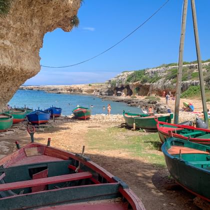 Kleurrijke houten boten op zandstrand in Polignano, Apulië. Rotsachtige kliffen omlijsten de baai met turquoise water en strandgangers.