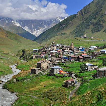 Dorp Ushguli genesteld in een groene vallei met traditionele stenen torens en huizen, omringd door besneeuwde Kaukasus bergen in Georgië.