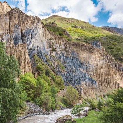 Dramatische riviervallei in Georgië met opvallende zeshoekige basaltrotsformaties op steile kliffen, omgeven door weelderige groene vegetatie.