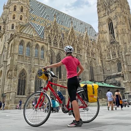 Fietser met rode toerfiets en gele fietstassen voor de Stephansdom in Wenen op een zonnige dag.