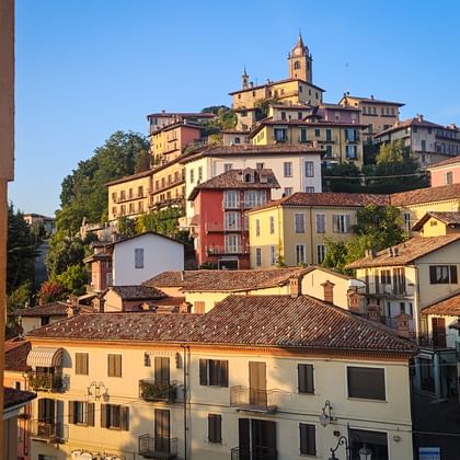 Kleurrijk heuvelplaatsje Monforte in Piemonte met meerlaagse gebouwen in warme tinten en kerk met klokkentoren op de top.
