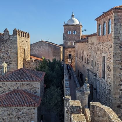 Middeleeuwse stenen vestingmuren en torens in Plasencia, Extremadura, met kantelen en rode pannendaken onder blauwe hemel.