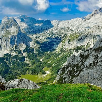 Dramatisch bergpanorama van de Julische Alpen met Triglav-top, toont kalksteenrotsen, groene valleien en alpenweiden onder blauwe lucht.