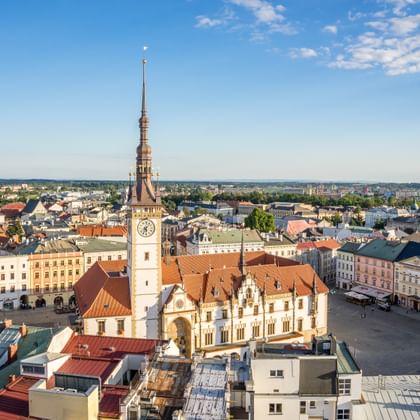Luchtfoto van het stadsplein van Olomouc met wit stadhuis en hoge klokkentoren. Historische gebouwen met rode daken rondom het plein.