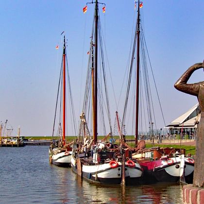 Traditionele zeilboten afgemeerd in de haven van Stavoren aan het IJsselmeer met een bronzen standbeeld van een vrouw op de voorgrond.