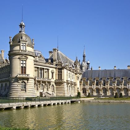Château de Chantilly in Oise, Frankrijk, toont Renaissance-architectuur met sierlijke torens en koepels weerspiegeld in het omringende water.