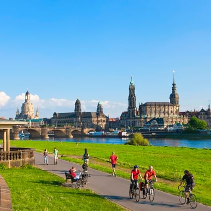 Fietsers op het Elbe fietspad bij Dresden met historische skyline inclusief kerktorens en barokke gebouwen aan de overkant.