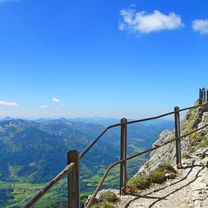 Rotsachtig bergpad met houten leuningen naar Wendelstein top, uitzicht op Beierse Alpen met groene valleien en blauwe lucht.