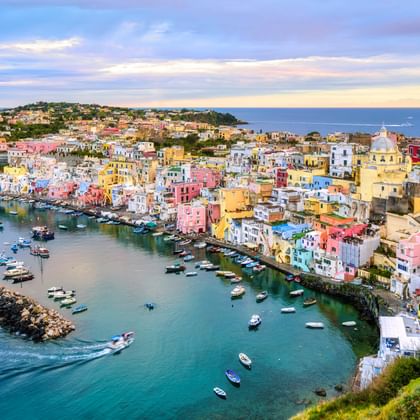 Luchtfoto van de kleurrijke haven van Procida met pastelkleurige huizen in roze, geel en blauw langs de waterkant. Boten in turquois water.