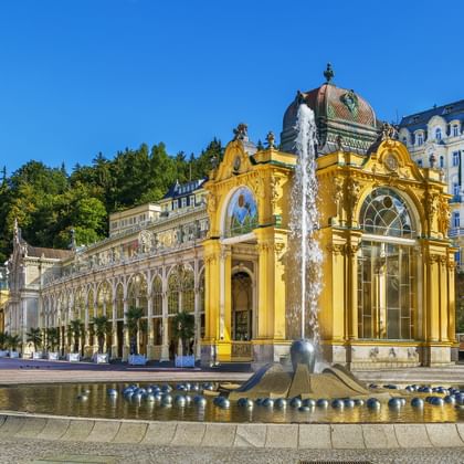 Gele barokke colonnade met fontein in Marianske Lazne. Het sierlijke gebouw heeft boogvensters en een decoratieve koepel onder blauwe lucht.