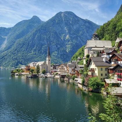 Hallstatt dorp met traditionele huizen en kerktoren aan de oever van een turquoise meer, omringd door groene beboste bergen.