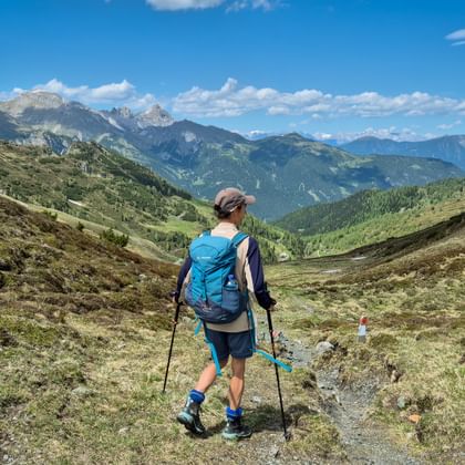 Vrouwelijke wandelaar met blauwe rugzak en wandelstokken op bergpad in Gschnitztal met Alpentoppen op de achtergrond.