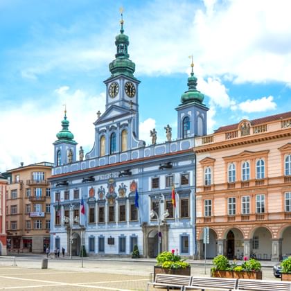 Hoofdplein in České Budějovice met barok stadhuis met blauwe gevel en twee torens met groene koperen koepels, omringd door kleurrijke gebouwen.
