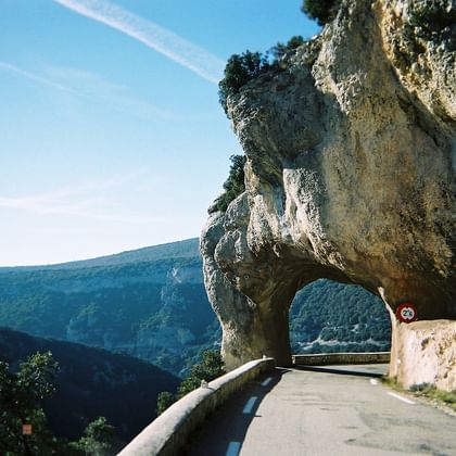Schilderachtige weg door natuurlijke kalkstenen boog in Gorges de la Nesque, Provence, met bergzicht en blauwe lucht.