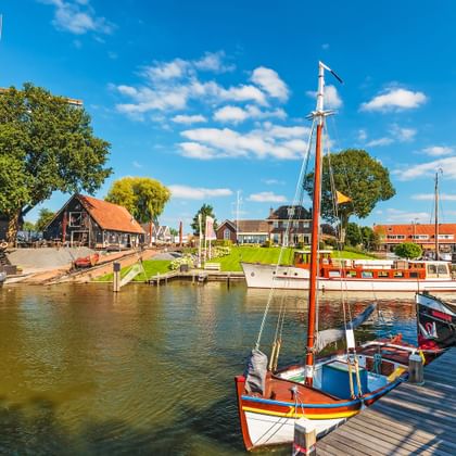 Kleurrijke traditionele zeilboten afgemeerd in een historische Nederlandse haven met rode pannendaken en houten steigers.