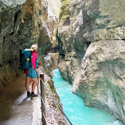 Wandelaarster met rugzak op houten looppad door Partnachklamm met turquoise water tussen kalkstenen wanden.