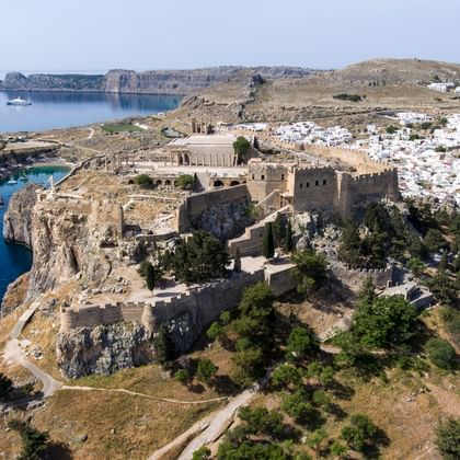 Luchtfoto van Lindos akropolisvesting op een rotsachtige heuvel met uitzicht op de Egeïsche Zee, met witte dorpshuizen en kustbaai op Rhodos.