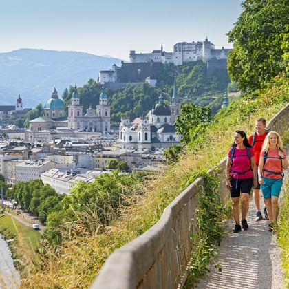 Drie wandelaars op het Mönchsberg-pad met panoramisch uitzicht op Salzburgs oude stad met barokke kerken en Hohensalzburg burcht.