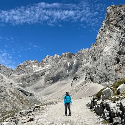 Persoon in blauwe jas staat op rotsachtig pad omringd door dramatische kalkstenen pieken in Picos de Europa, Asturië, Spanje.