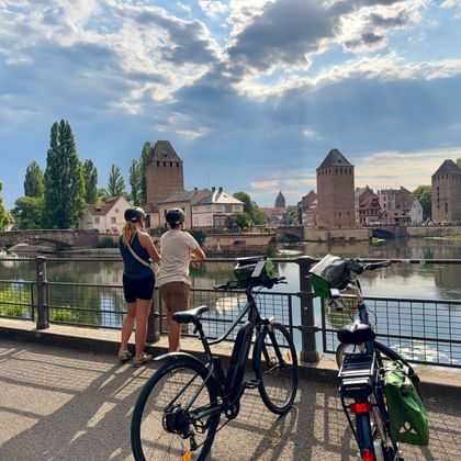 Twee fietsers met fietsen bekijken de middeleeuwse torens van Ponts Couverts over het kanaal in Straatsburg onder een dramatische bewolkte hemel.